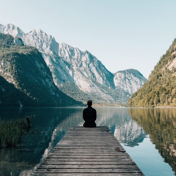 Person sitting by a lake with mountains